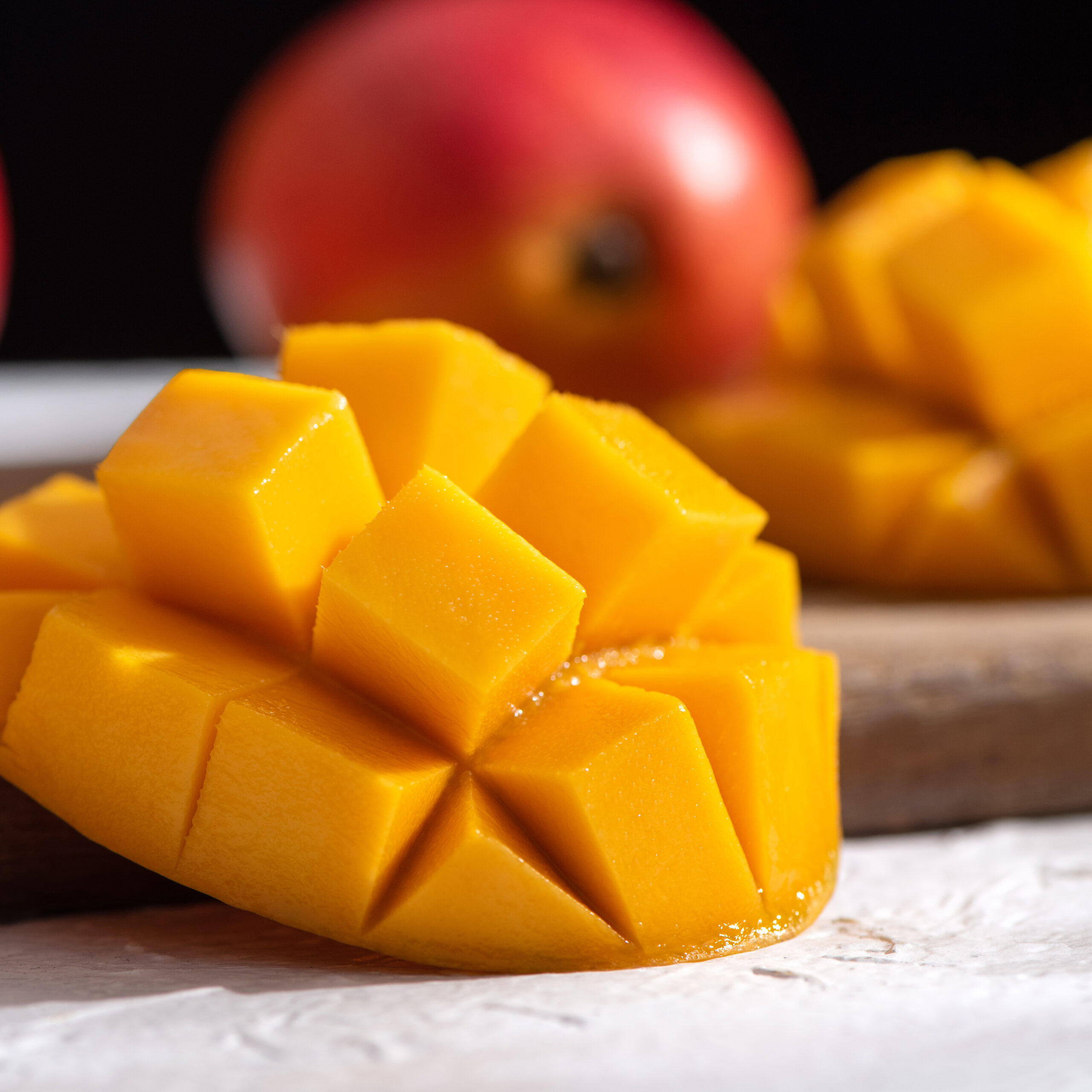Diced fresh mango fruit on wooden cutting board with sunlight and leaf shadow at home kitchen in the afternoon.